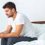 Man sitting on bed, looking pensive.