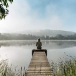 Image of a woman sitting at the end of a dock looking into the distance thinking about her window of tolerance.