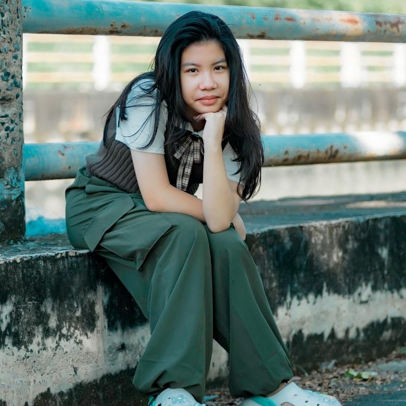 Teen sitting by a railing outdoors.